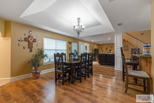 dining area featuring hardwood / wood-style floors, a notable chandelier, and a raised ceiling