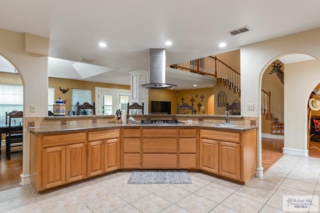 kitchen with stone counters, sink, stainless steel gas cooktop, exhaust hood, and kitchen peninsula