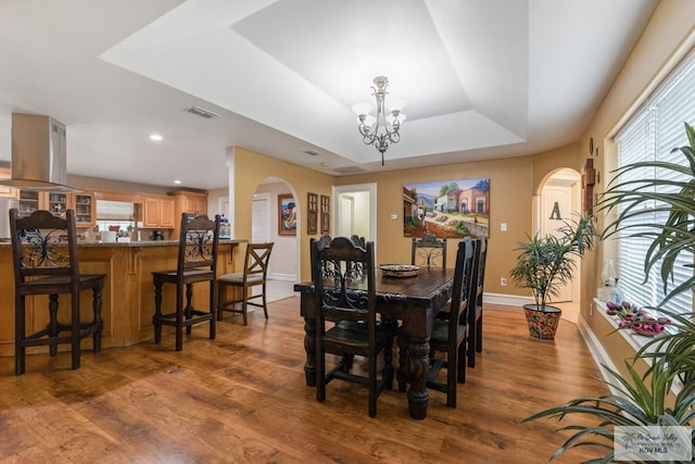 dining space featuring an inviting chandelier, hardwood / wood-style floors, and a raised ceiling