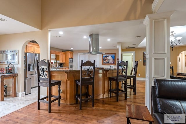 kitchen featuring a breakfast bar, stone counters, appliances with stainless steel finishes, island exhaust hood, and kitchen peninsula