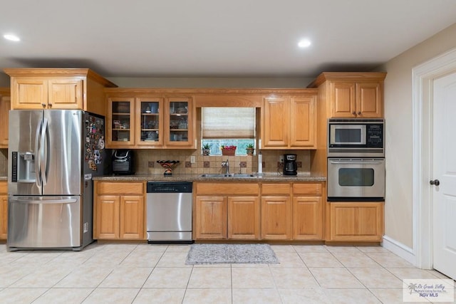 kitchen featuring sink, stone counters, appliances with stainless steel finishes, backsplash, and light tile patterned flooring