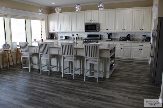 kitchen featuring pendant lighting, a kitchen island with sink, white cabinets, ornamental molding, and stainless steel appliances