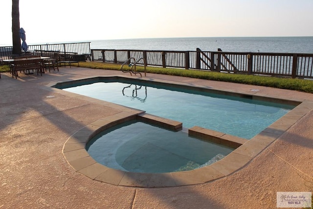 view of swimming pool featuring an in ground hot tub, a water view, and a patio