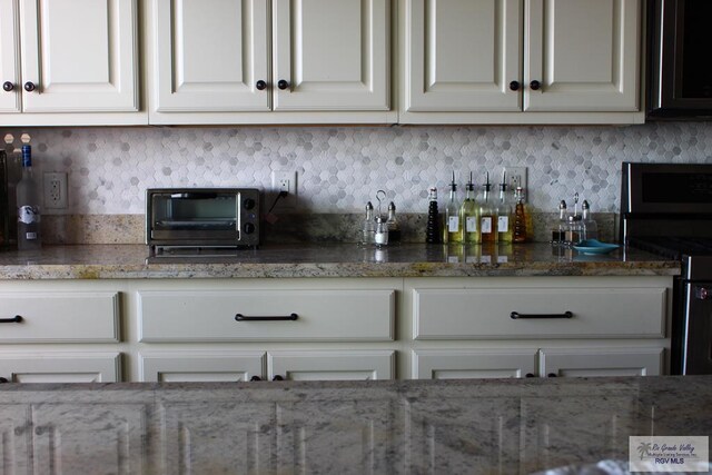 kitchen with stone counters, white cabinetry, black stove, and decorative backsplash