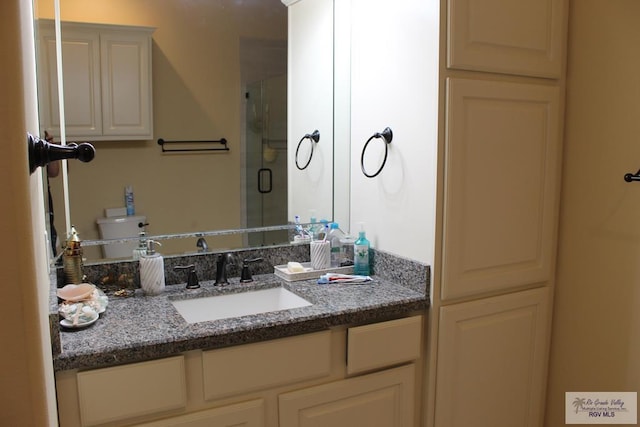 bathroom featuring a shower with door, vanity, and toilet