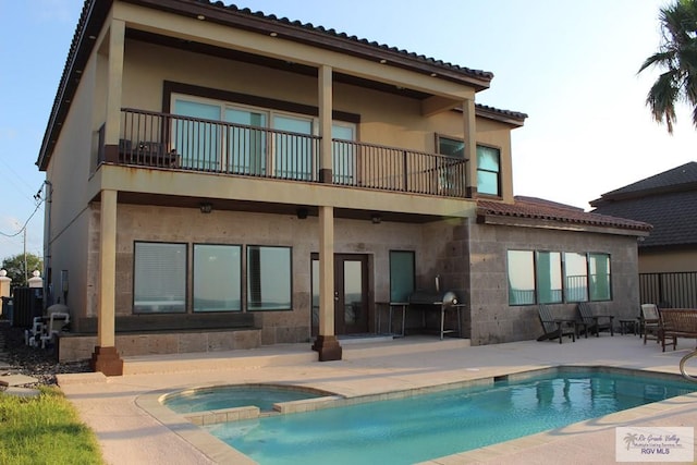 rear view of house with a patio, a balcony, and a pool with hot tub