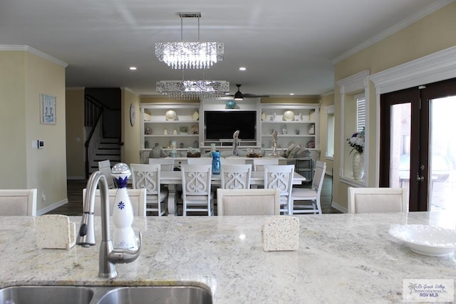 kitchen featuring sink, hanging light fixtures, light stone counters, crown molding, and wood-type flooring