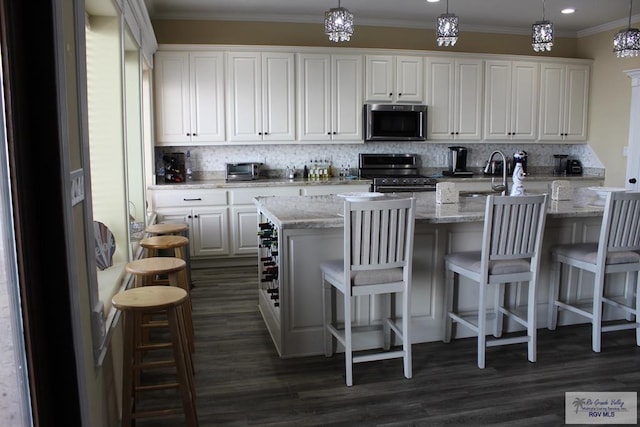 kitchen featuring appliances with stainless steel finishes, tasteful backsplash, pendant lighting, white cabinets, and a breakfast bar area