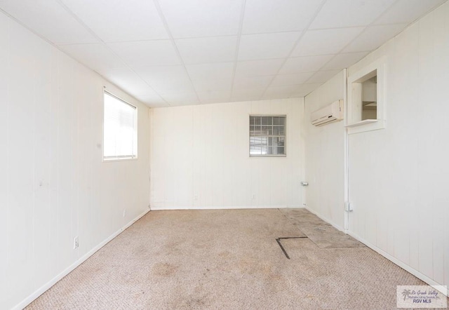 empty room with a wall unit AC, light carpet, and a drop ceiling