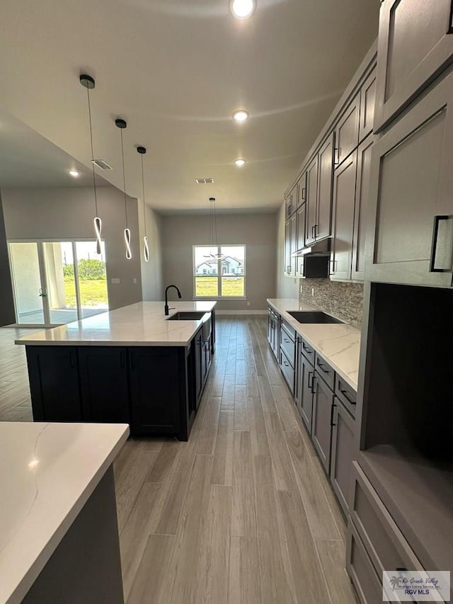 kitchen featuring light stone countertops, black electric stovetop, sink, decorative light fixtures, and light hardwood / wood-style flooring