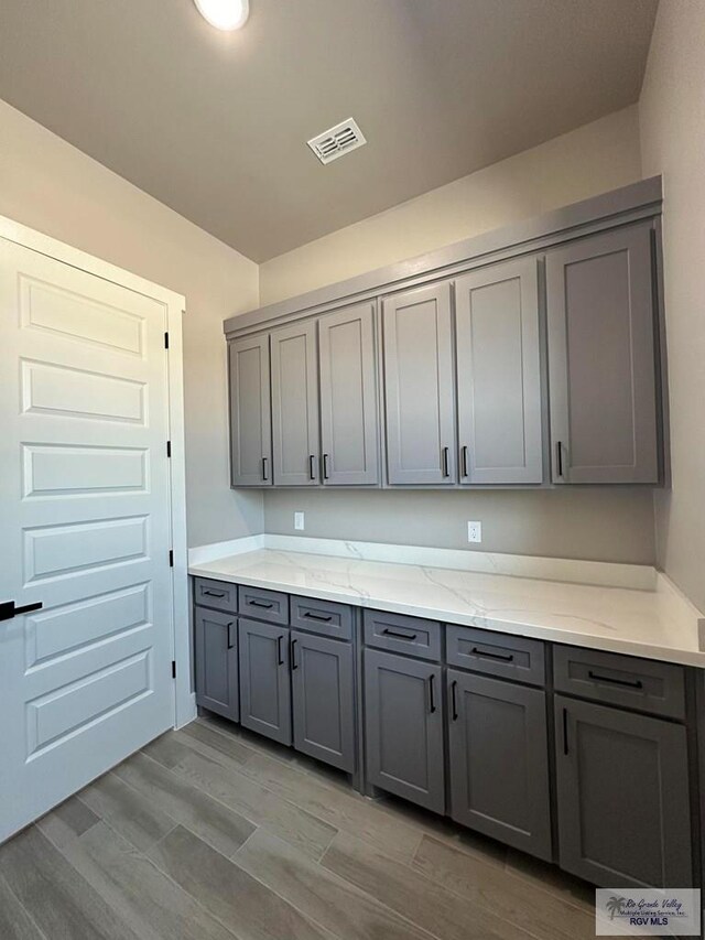 kitchen featuring light hardwood / wood-style floors, light stone countertops, and gray cabinetry