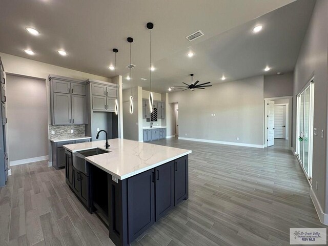 kitchen with a large island, sink, ceiling fan, hardwood / wood-style floors, and pendant lighting