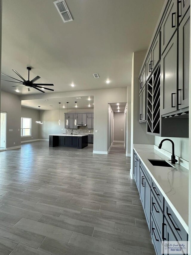 kitchen with gray cabinetry, light stone countertops, sink, wood-type flooring, and decorative backsplash