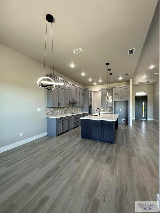 kitchen featuring a center island with sink, hardwood / wood-style floors, pendant lighting, gray cabinets, and tasteful backsplash