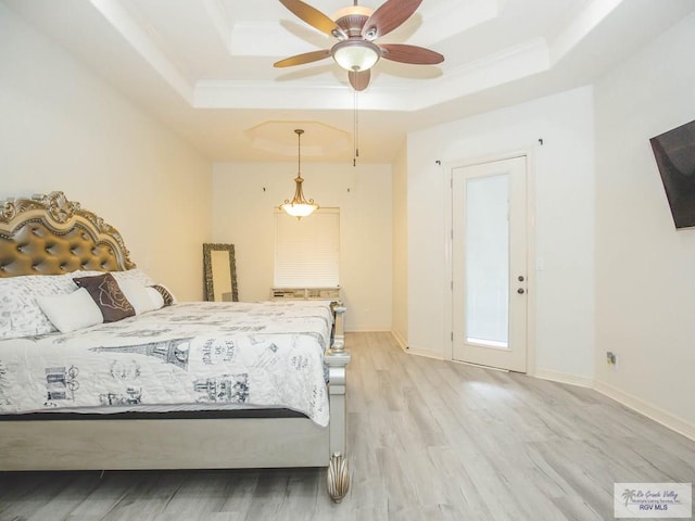 bedroom with a raised ceiling, ceiling fan, and light wood-type flooring