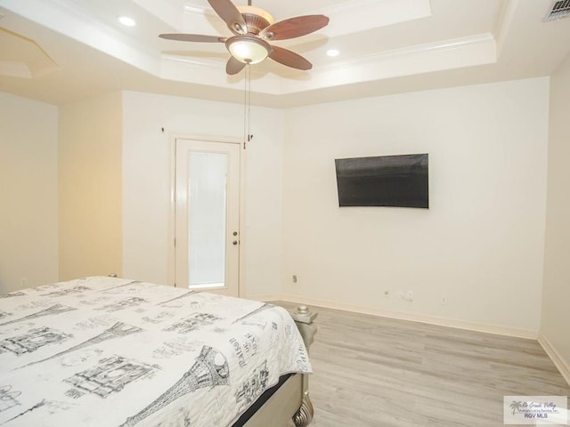 bedroom with ceiling fan, light wood-type flooring, and a tray ceiling