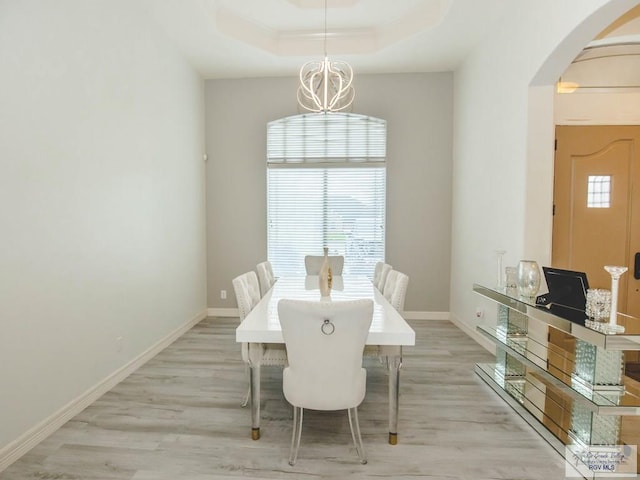 dining area with a raised ceiling, a chandelier, and light hardwood / wood-style floors