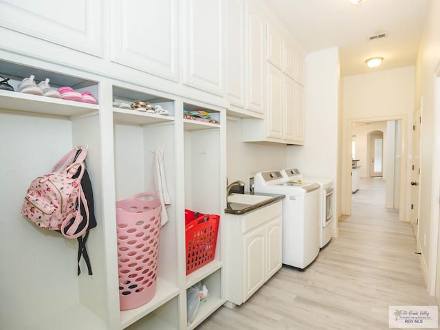 clothes washing area with cabinets, washing machine and dryer, light hardwood / wood-style flooring, and sink