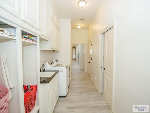 laundry room featuring cabinets, washing machine and dryer, and light hardwood / wood-style flooring