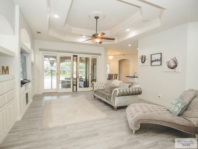 living room with ceiling fan, light hardwood / wood-style floors, and a raised ceiling