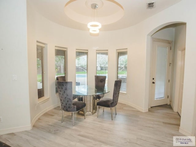 dining area with light wood-type flooring and a raised ceiling