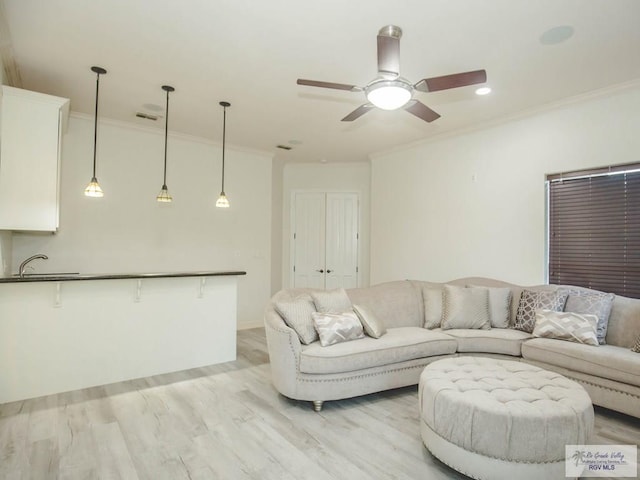 living room featuring ceiling fan, ornamental molding, sink, and light hardwood / wood-style flooring