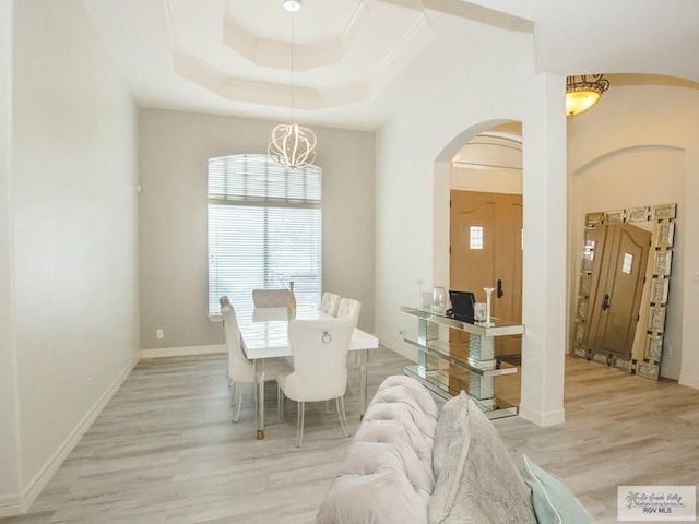 dining space featuring light hardwood / wood-style floors, an inviting chandelier, and a tray ceiling