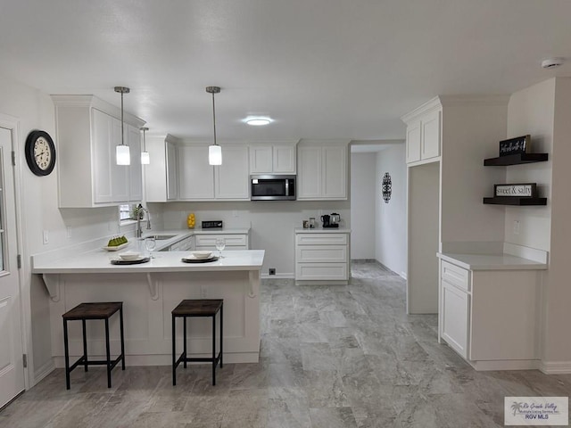 kitchen with kitchen peninsula, sink, decorative light fixtures, a kitchen bar, and white cabinetry