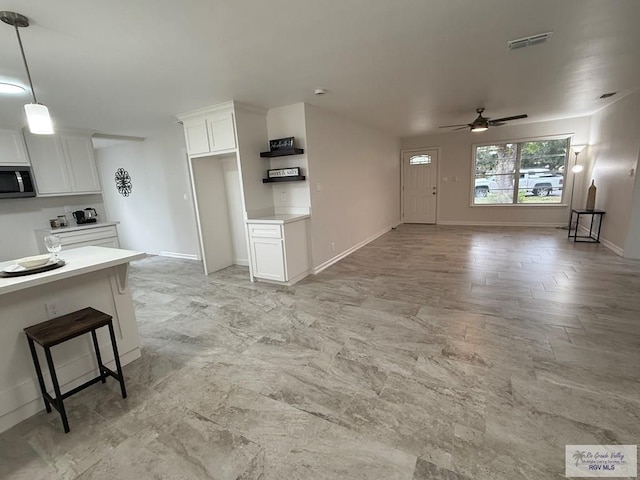 interior space with a kitchen breakfast bar, decorative light fixtures, white cabinetry, and ceiling fan