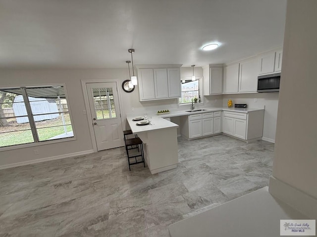 kitchen featuring sink, decorative light fixtures, a center island, white cabinetry, and a breakfast bar area