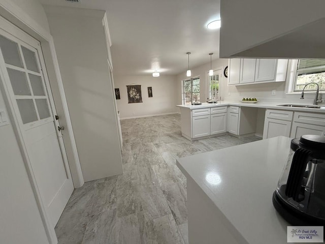 kitchen featuring white cabinetry, sink, light hardwood / wood-style flooring, kitchen peninsula, and decorative light fixtures