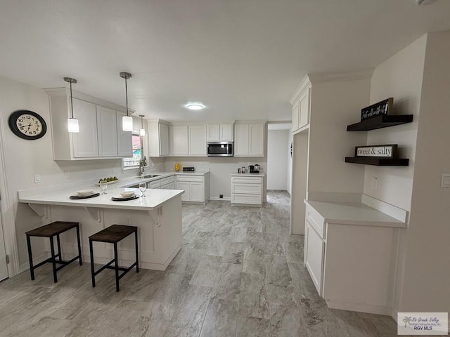 kitchen featuring white cabinets, sink, hanging light fixtures, a kitchen bar, and kitchen peninsula