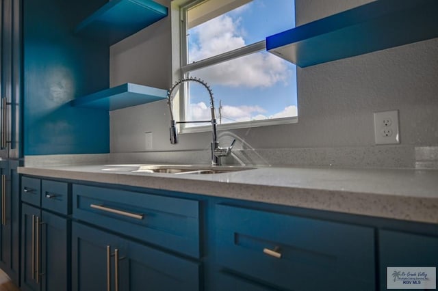 kitchen featuring a healthy amount of sunlight, light stone counters, blue cabinets, and sink