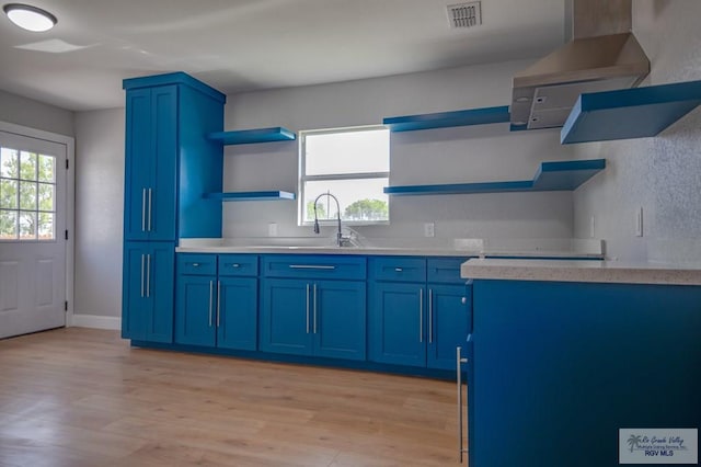 kitchen featuring blue cabinetry, sink, exhaust hood, and light wood-type flooring