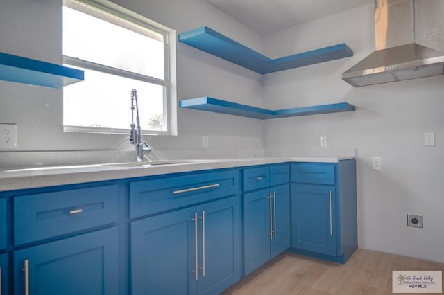 kitchen featuring light hardwood / wood-style floors, blue cabinets, and wall chimney range hood