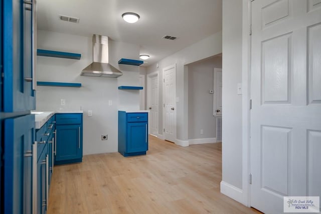 kitchen with light hardwood / wood-style flooring, wall chimney range hood, and blue cabinets