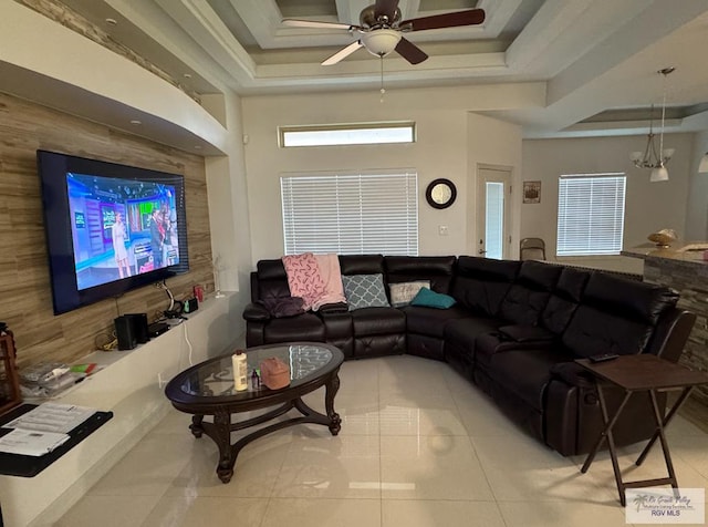 tiled living room with ceiling fan with notable chandelier, a tray ceiling, and ornamental molding