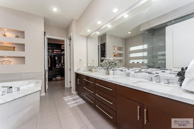 full bath with double vanity, a sink, a walk in closet, tile patterned flooring, and a shower stall