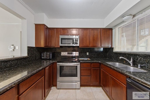 kitchen with light tile patterned flooring, sink, stainless steel appliances, and dark stone countertops