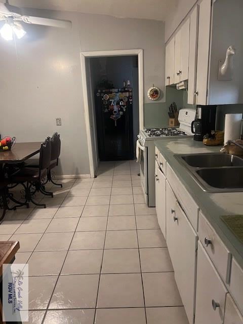 kitchen featuring sink, light tile patterned floors, stainless steel gas range, black fridge, and white cabinets