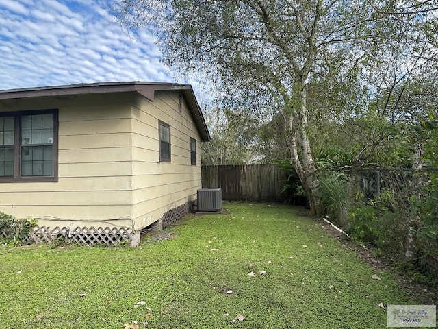 view of property exterior with central AC, fence, and a yard