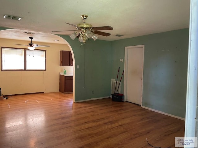 unfurnished living room featuring light wood finished floors, arched walkways, ceiling fan, and visible vents