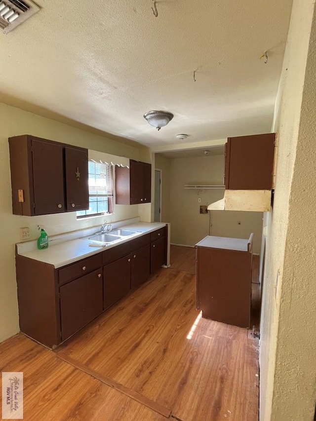 kitchen featuring light wood-style flooring, dark brown cabinets, a sink, visible vents, and a textured ceiling