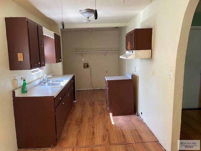 laundry area featuring light wood finished floors, arched walkways, and a sink