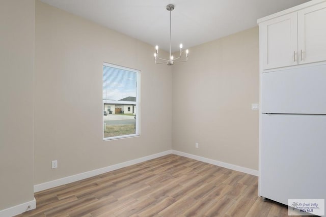 unfurnished dining area featuring a chandelier and light hardwood / wood-style flooring