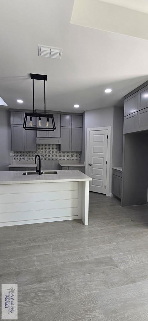 kitchen with visible vents, a sink, gray cabinets, light countertops, and backsplash