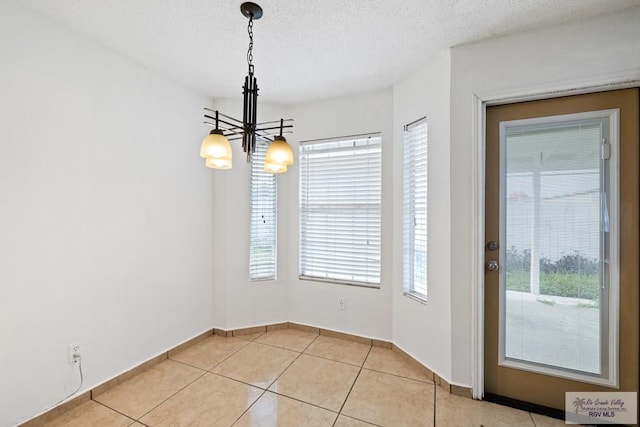 unfurnished dining area featuring light tile patterned floors, a textured ceiling, and a notable chandelier