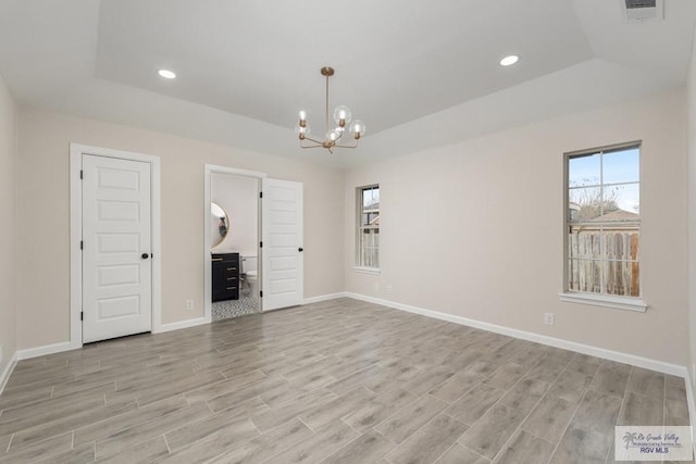 spare room with a raised ceiling and an inviting chandelier