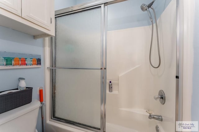 bathroom featuring toilet and combined bath / shower with glass door