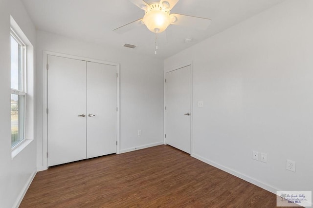 unfurnished bedroom featuring dark wood-type flooring, ceiling fan, a closet, and multiple windows